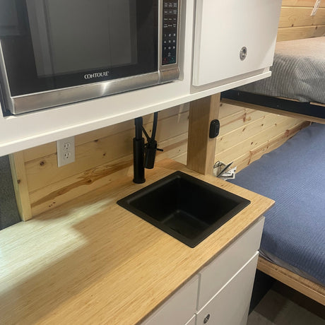RV rental kitchen: compact microwave, black sink, wood counter, and bunk beds in the background.