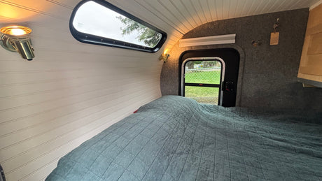 This RV rental offers a cozy bedroom with a quilted bed, a window view, and warm sconce lighting for comfortable travel.