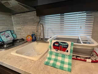 Compact kitchen in an RV rental, featuring a sink, stove, and space-saving dish rack. Ready for your next travel adventure!