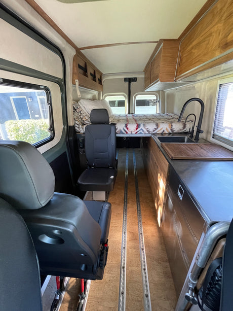 RV rental interior: Front seats lead to a rear bed and a kitchen with sink and wood cabinets, perfect for van life.