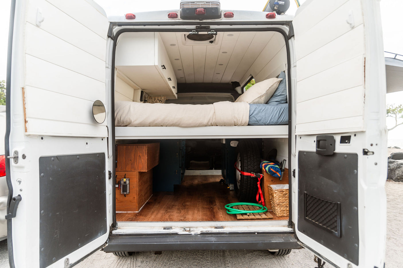 Rear view of an RV rental: a custom camper van interior with a bed, white cabinets, and organized storage under the bed.