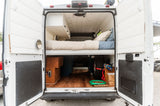 Rear view of an RV rental: a custom camper van interior with a bed, white cabinets, and organized storage under the bed.