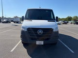 Front of a white Mercedes-Benz Sprinter van, often used for RV rental conversions, parked in a sunny lot.