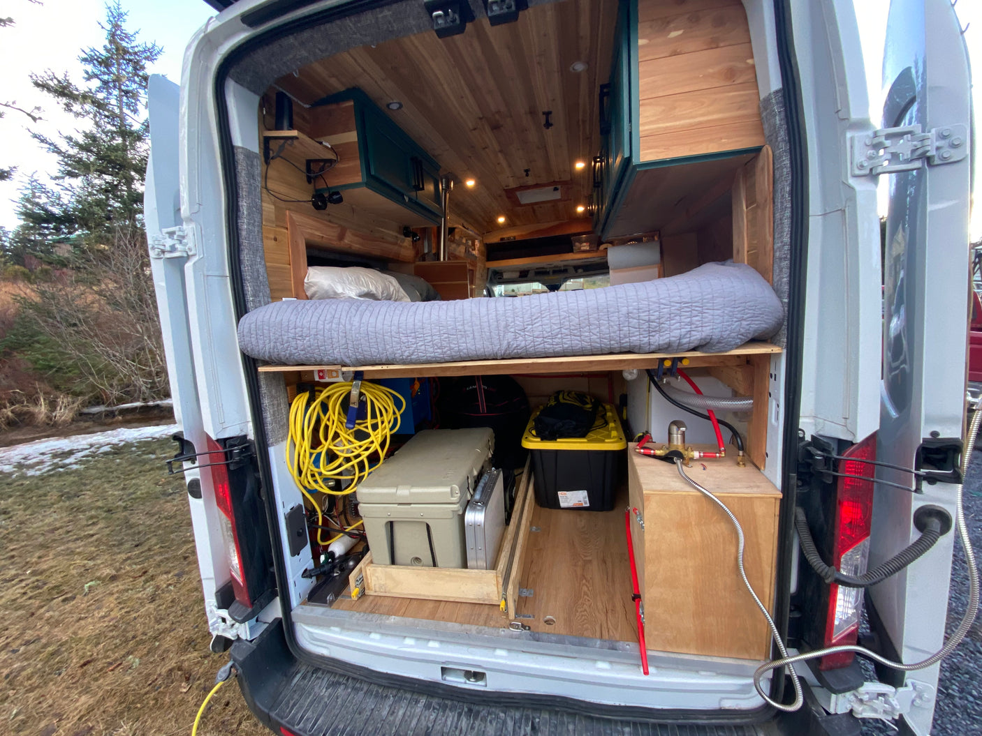 RV rental camper van's open rear reveals a custom interior with bed, storage, and water system for adventure.