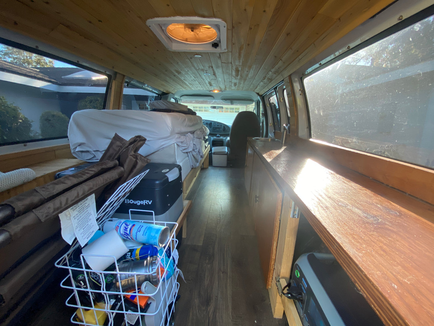 Explore this rv rental camper van's interior: wood-paneled, with a cozy bed, sink area, and organized storage.