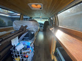 Explore this rv rental camper van's interior: wood-paneled, with a cozy bed, sink area, and organized storage.