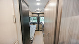 RV rental interior: Hallway view of a cozy camper van with a bed, refrigerator, and light wood cabinets.