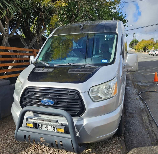 A custom silver Ford Transit camper van, an excellent RV rental. Features a black hood & bull bar. License RJL-6018.