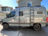 Adventure-ready gray camper van with ladder & roof rack. Ideal for your next RV rental road trip.