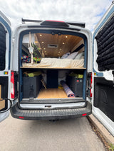 RV rental: Rear view of a customized camper van interior with bed and storage, doors open.