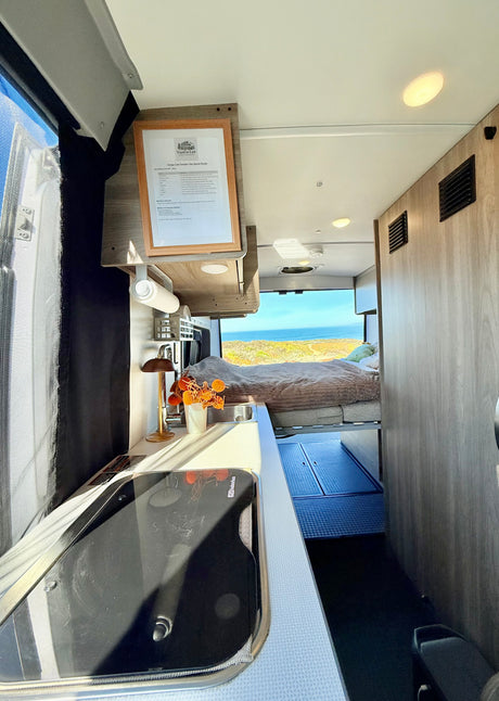 Vango Lee rv rental camper van interior: kitchenette, elevated bed, and panoramic ocean view from the rear.