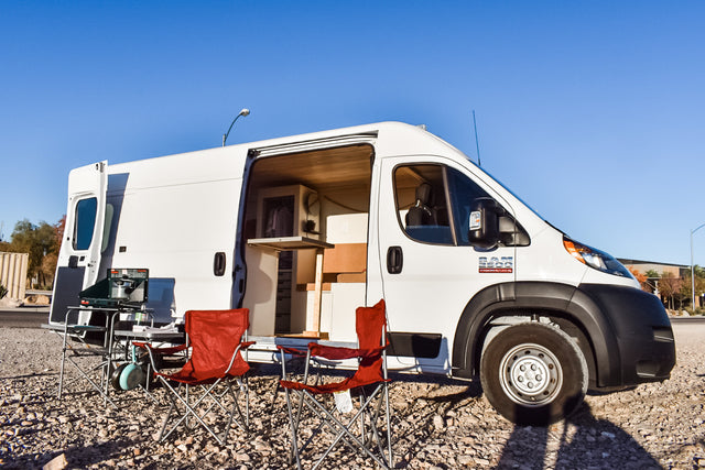 This white camper van, an ideal RV rental, showcases its comfortable interior and outdoor camping setup with chairs and stove.