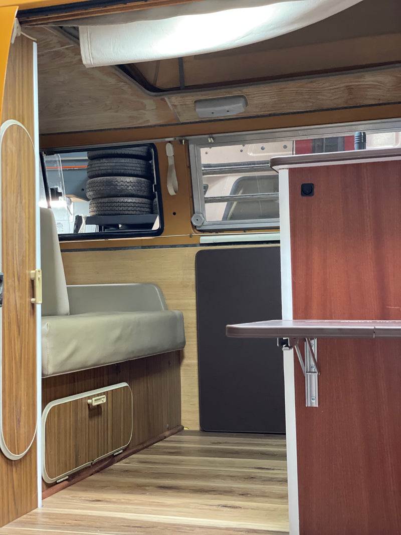 RV rental interior showcasing warm wood paneling, a versatile seating area, overhead storage, and a clever compartment for tires. — photo 5