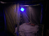 Cozy RV rental sleeping space for camping, featuring a bed, plaid pillows, blue lantern, and string lights.