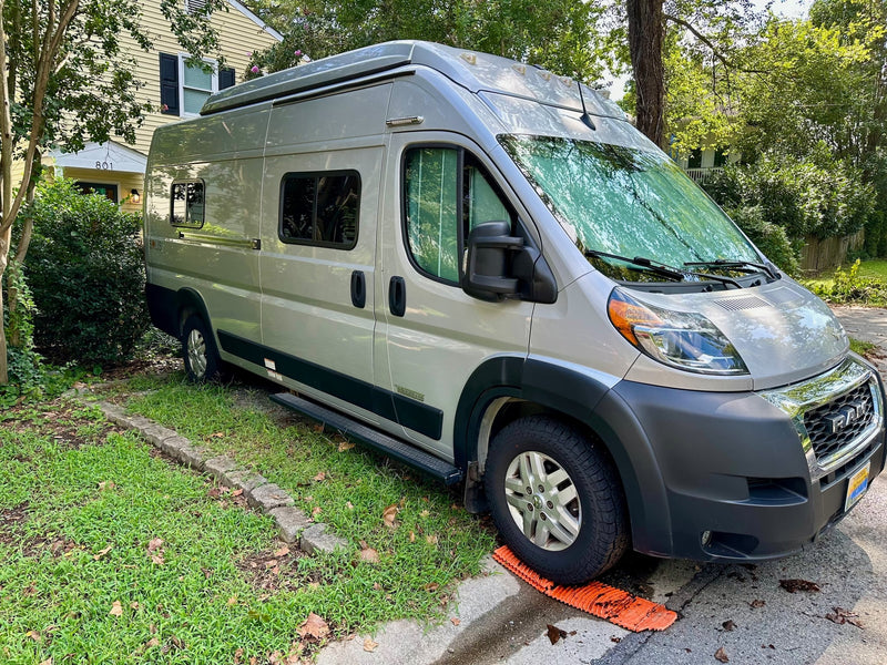  with shadows on its side and an orange mat under the front wheel.|Front view of a silver Ram ProMaster Winnebago RV rental — photo 4