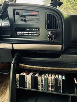 Classic RV rental dashboard with a cassette player and a built-in shelf displaying a collection of audio tapes.