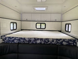 This RV rental offers a comfortable sleeping space with a wide bed, floral cover, black sofa, and white cabinets.
