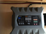 A gray PRO-LOGIX PL2320 battery charger, displaying its control panel, is mounted on a light wood wall. Essential for an rv rental power system.
