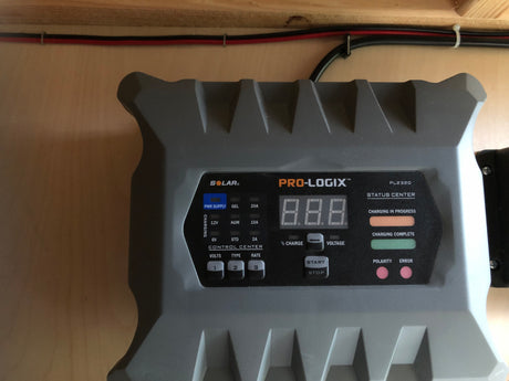 A gray PRO-LOGIX PL2320 battery charger, displaying its control panel, is mounted on a light wood wall. Essential for an rv rental power system.