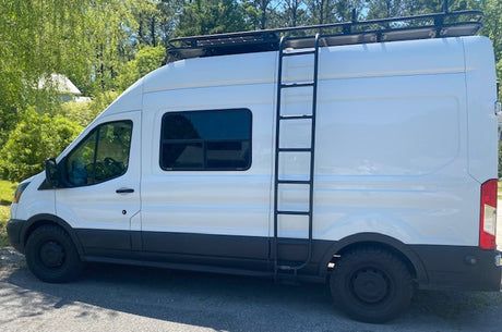 Side view of a white converted van, featuring a roof rack, ladder, and all-terrain tires. Your ultimate rv rental.