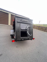 Black compact RV rental, rear view with door, window, red tail lights. Parked near storage units, a "Wrong Way" sign visible.