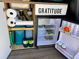 RV rental kitchen setup: compact sink, mini-fridge, water tanks, and paper towels for organized camper living.