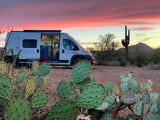 An RV rental parked in a vibrant desert sunset, surrounded by saguaro and prickly pear cacti, ideal for camping.