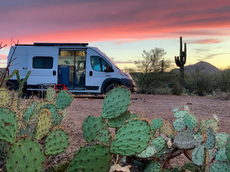 An RV rental parked in a vibrant desert sunset, surrounded by saguaro and prickly pear cacti, ideal for camping.