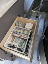 Open RV rental kitchen drawer revealing compact, colorful utensils, a corkscrew, and cooking tools.