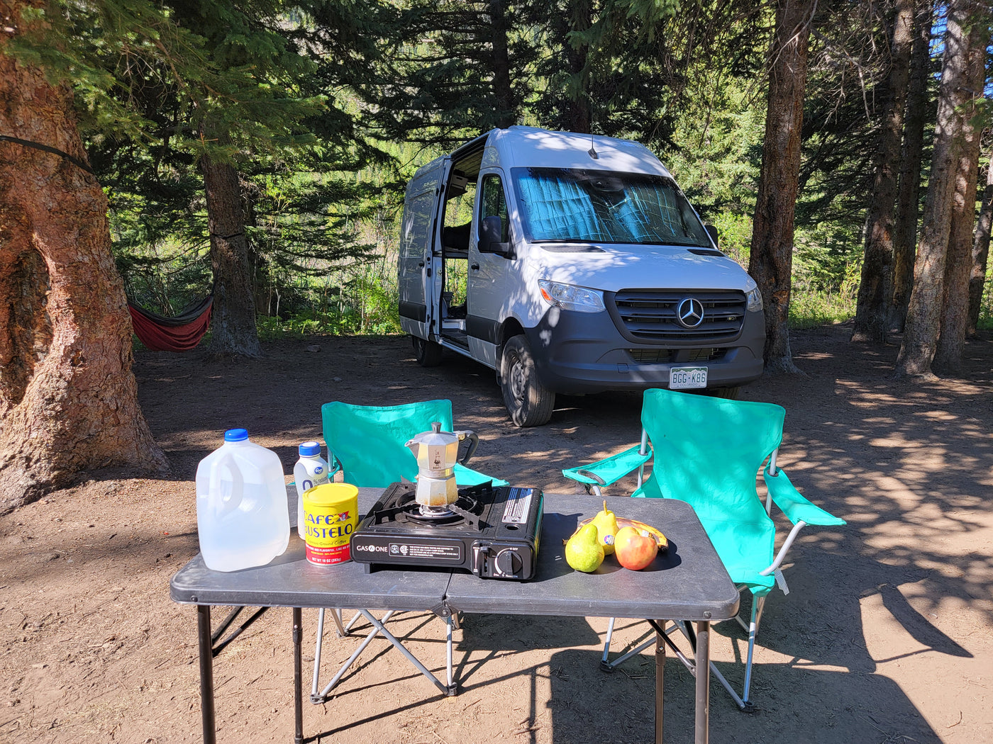 RV rental adventure: A Sprinter van camper at a serene forest campsite with a coffee setup, fruit, and chairs. — photo 5