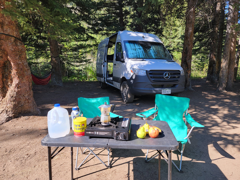 RV rental adventure: A Sprinter van camper at a serene forest campsite with a coffee setup, fruit, and chairs. — photo 5
