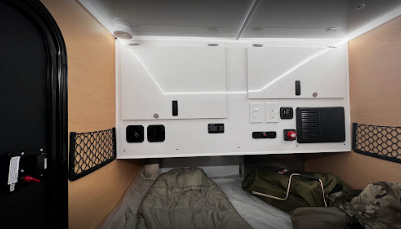 rv rental camper interior: wood walls, overhead cabinets with LED lights, control panel, mesh storage, and comfortable sleeping area.