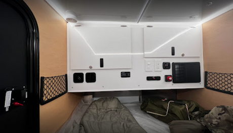 rv rental camper interior: wood walls, overhead cabinets with LED lights, control panel, mesh storage, and comfortable sleeping area.