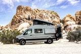 Explore with this grey RV rental camper van, featuring a pop-top tent, parked among desert rocks. Ideal for outdoor adventures.