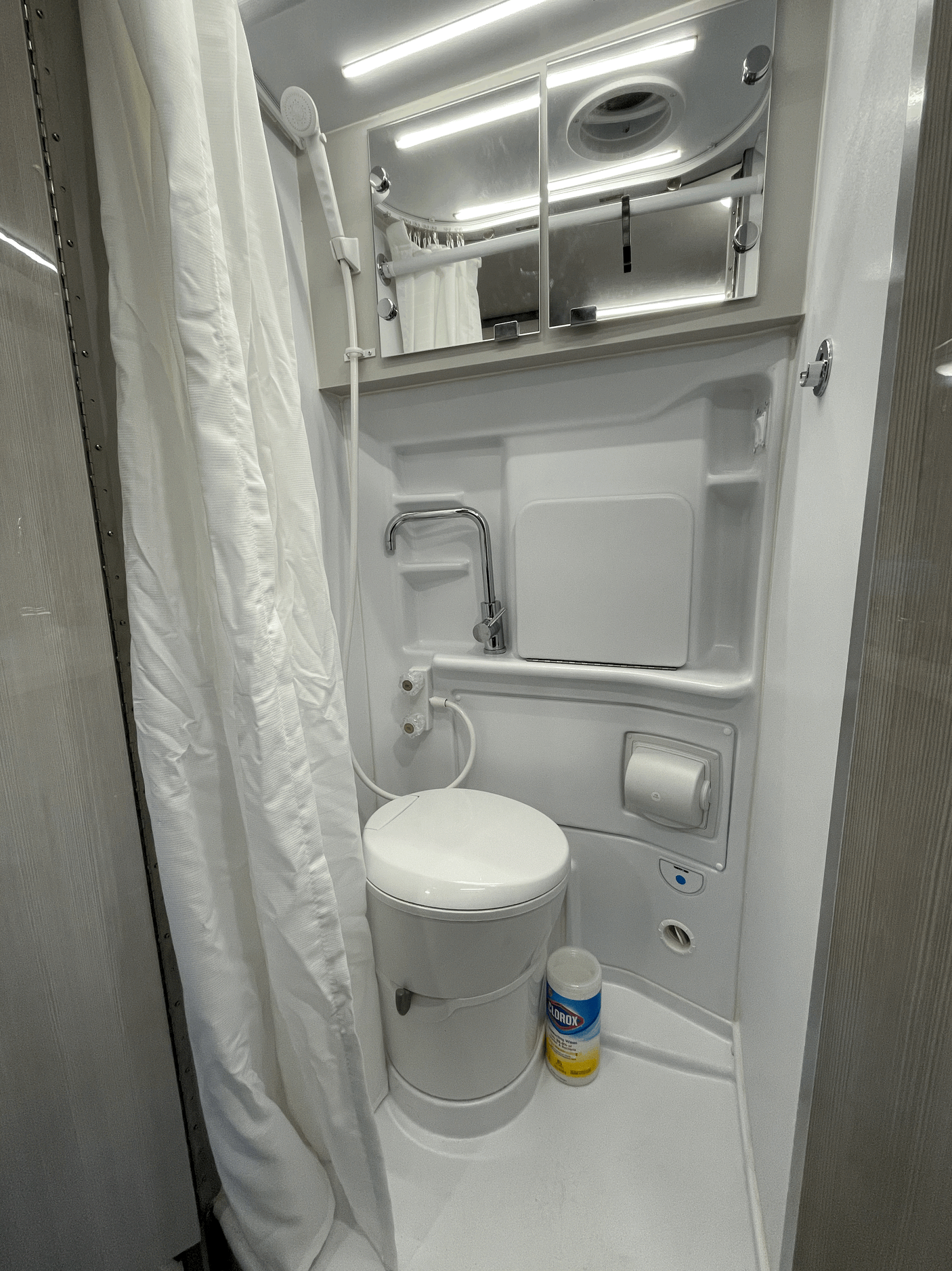 Bright RV rental wet bath: white toilet, shower, and mirrored cabinet for efficient use of space.