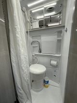 Bright RV rental wet bath: white toilet, shower, and mirrored cabinet for efficient use of space.