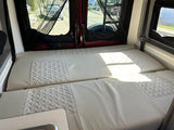 Interior of an RV rental showing a comfortable bed. Sunlight illuminates the quilted cushions, perfect for travel & adventure.