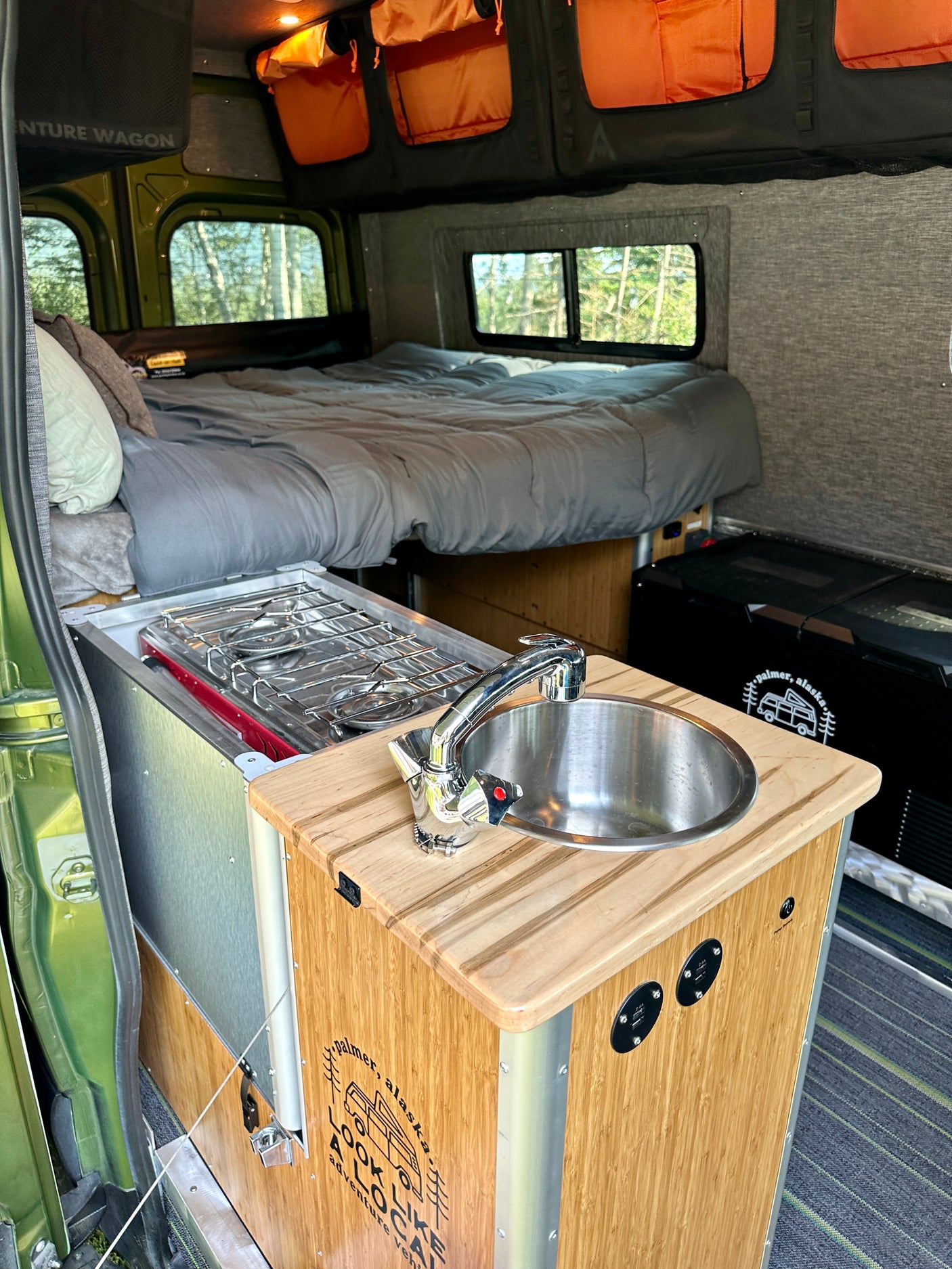 Explore this RV rental's inviting interior: a comfy bed, functional kitchen with stove & sink, plus overhead storage.