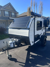This small white and black SUNRAY SPORT RV rental, featuring solar panels, is parked on asphalt, ready for your next trip.