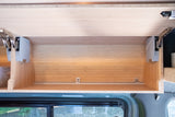 Open bamboo overhead cabinet in an RV rental, featuring gas struts and a bottom rail for secure storage.