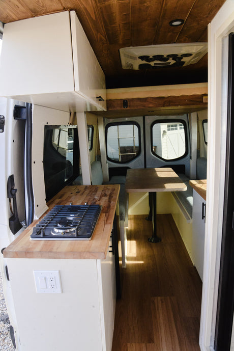 This bright RV rental interior showcases a compact kitchen with a stove, wooden countertops, and a cozy dining area, perfect for adventurers.