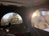 Cozy inside an RV rental with panoramic mountain and forest views. Legs visible, enjoying a bright, snowy outdoor escape.
