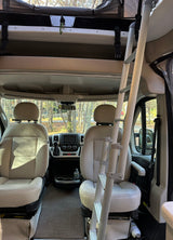 Inside an RV rental, showing the driver's cabin with front seats, dashboard, and an overhead bunk ladder.
