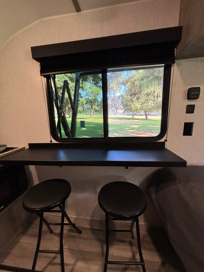 Enjoy the view from this RV rental's cozy window desk with two bar stools, overlooking a serene park. — photo 10