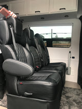 Luxury RV rental interior featuring plush black leather captain's chairs with white stitching, overhead cabinets, and a window view.