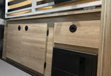 RV rental interior: Light wood cabinetry with flush handles, a power center, and a hinged bed frame maximizing space.