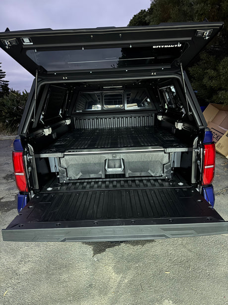 Open pickup truck bed with camper shell, revealing a DECKED drawer storage system, ideal for a compact RV rental trip.