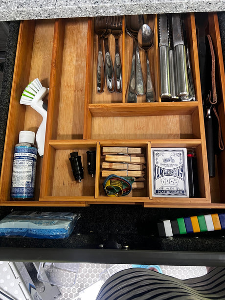 This organized RV rental kitchen drawer holds cutlery, soap, brush, playing cards, and travel essentials for compact living.
