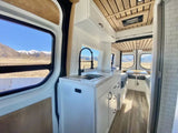 This RV rental offers a modern camper van interior with a kitchen, dining, and scenic mountain views.