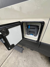 RV rental: Exterior hatch open on a cream van, revealing a grey/blue portable toilet cassette for waste disposal.